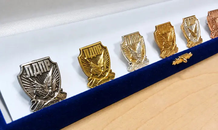 Emblemer i guld og sølv med relief, vist på en blå displayholder