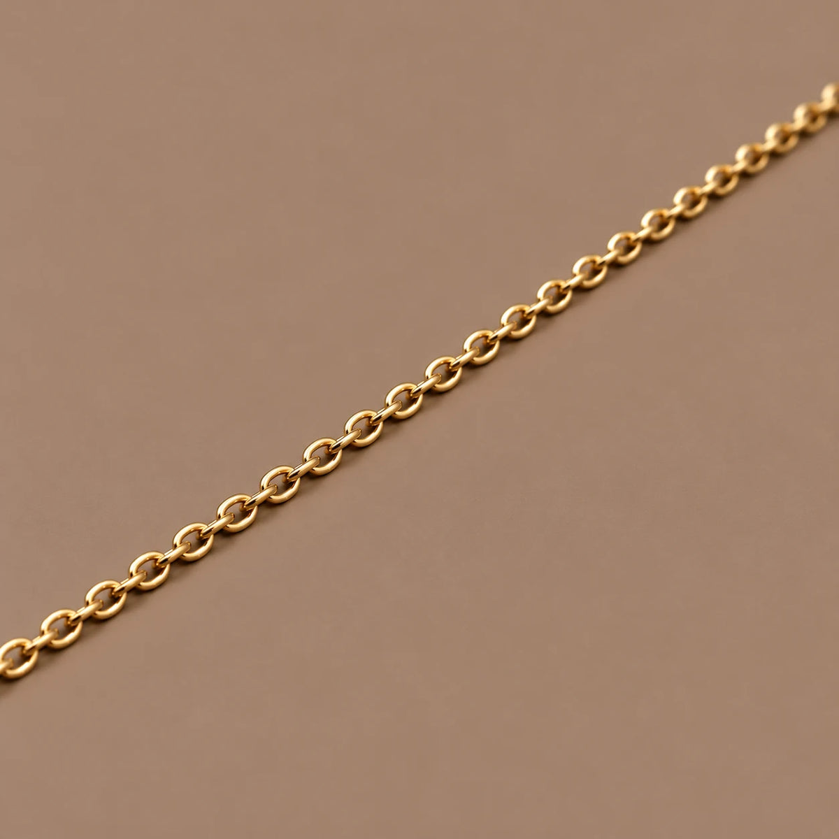 Ankerkæde i 18 kt gult guld, 1,5 mm, med ovale led på taupe baggrund.
