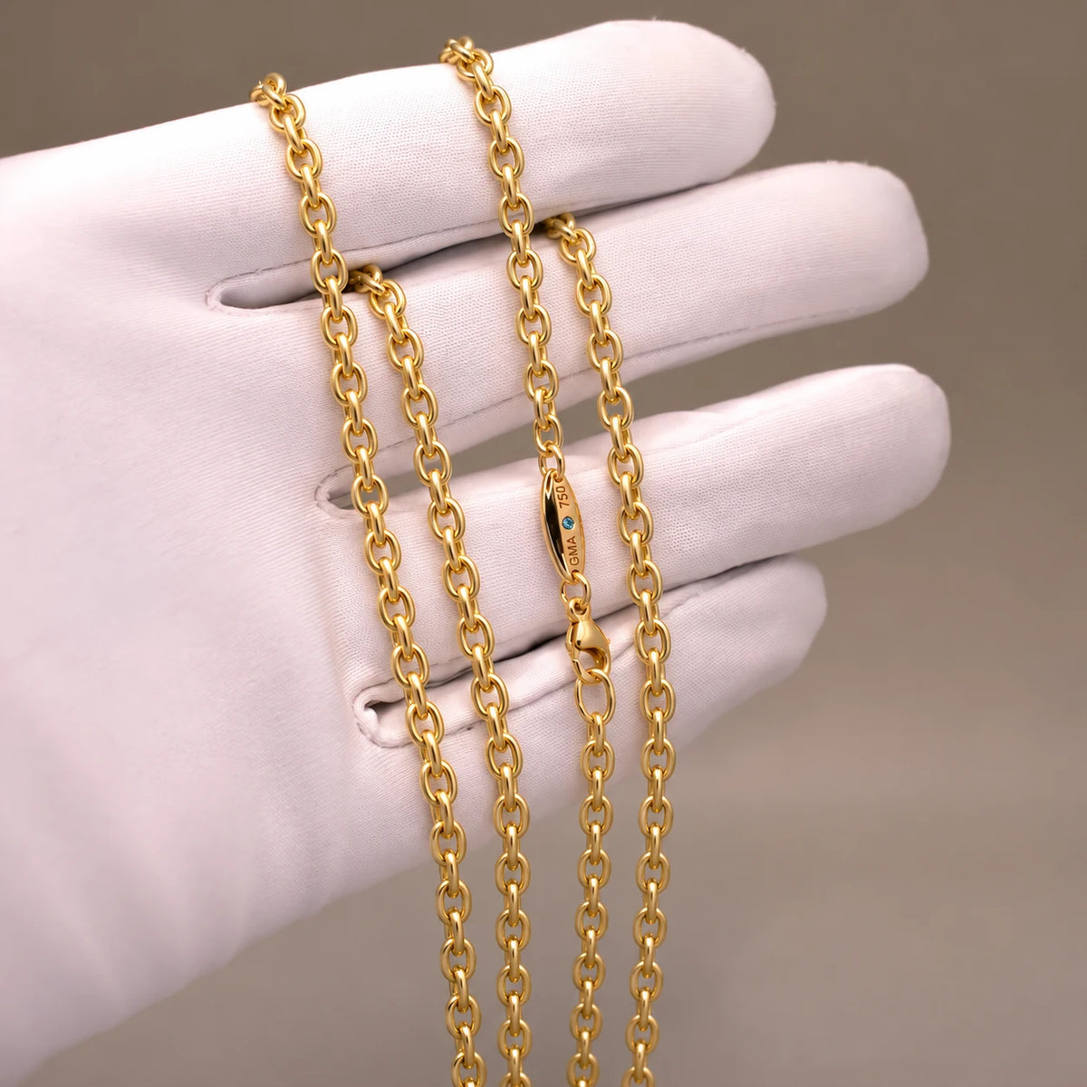 Ankerkæde i 18 kt gult guld, 3 mm, på hvid handske med blå diamant ved låsen.