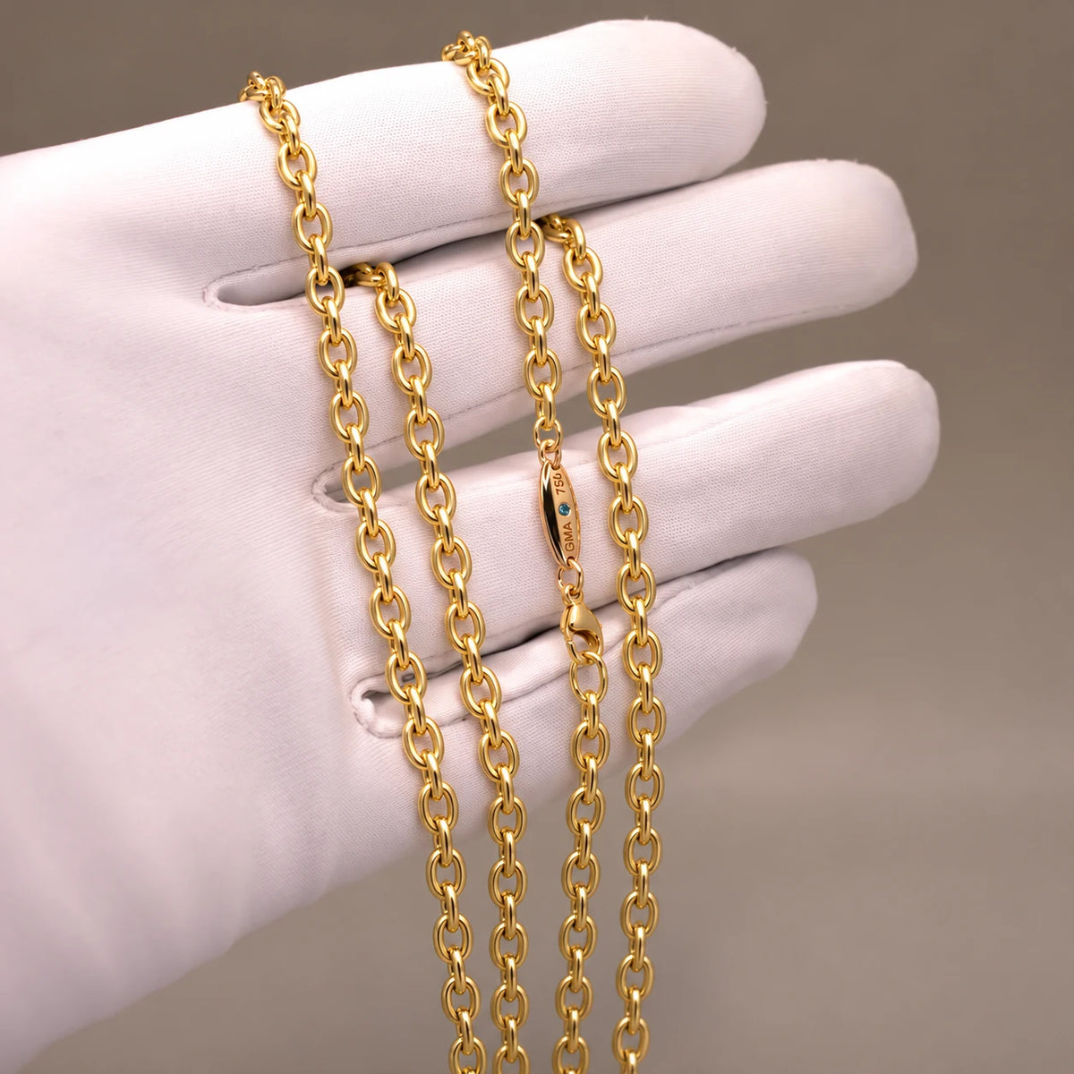 Ankerkæde i 18 kt gult guld, 4,2 mm, på hvid handske med blå diamant ved låsen.