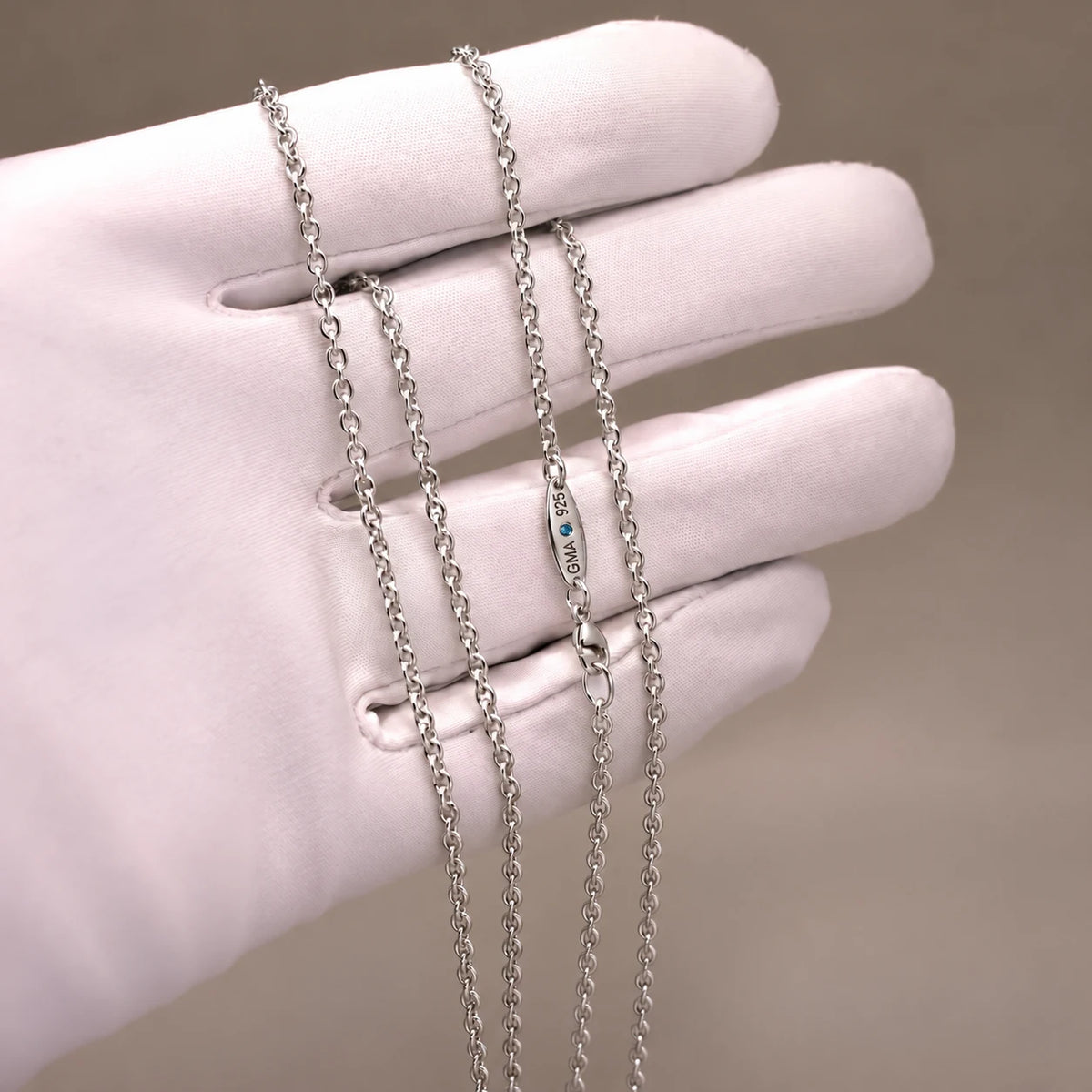 Ankerkæde i 925 sterlingsølv på hvid handske med GMA-stempel og blå diamant ved låsen.
