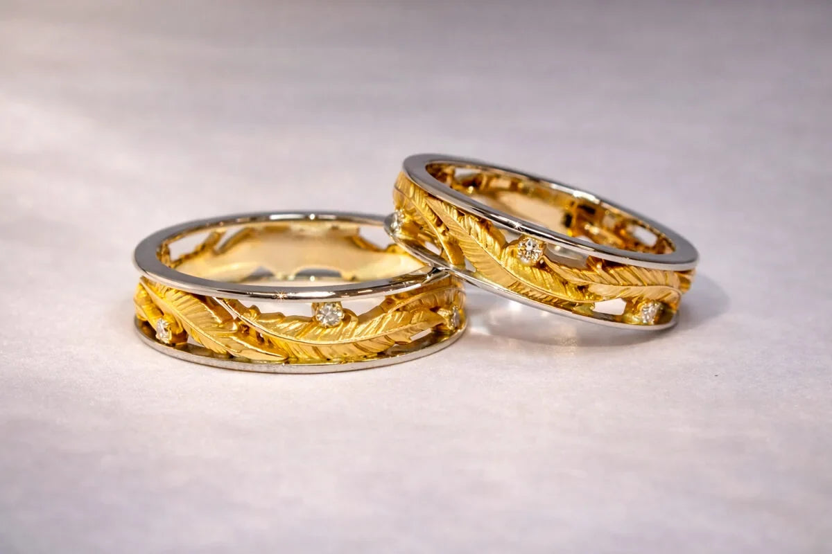 To vielsesringe med fjermotiver i gult guld, diamanter og sidekanter i hvidguld