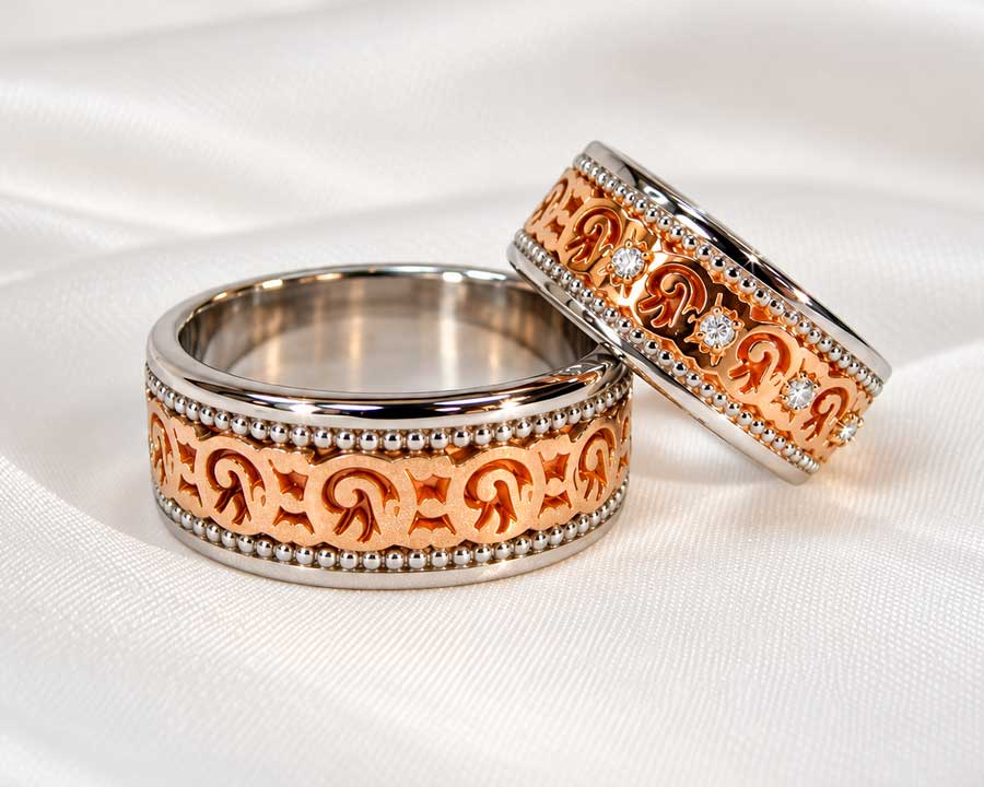Brede vielsesringe i rosaguld og hvidguld med slyngede ornamenter og diamanter i hendes ring