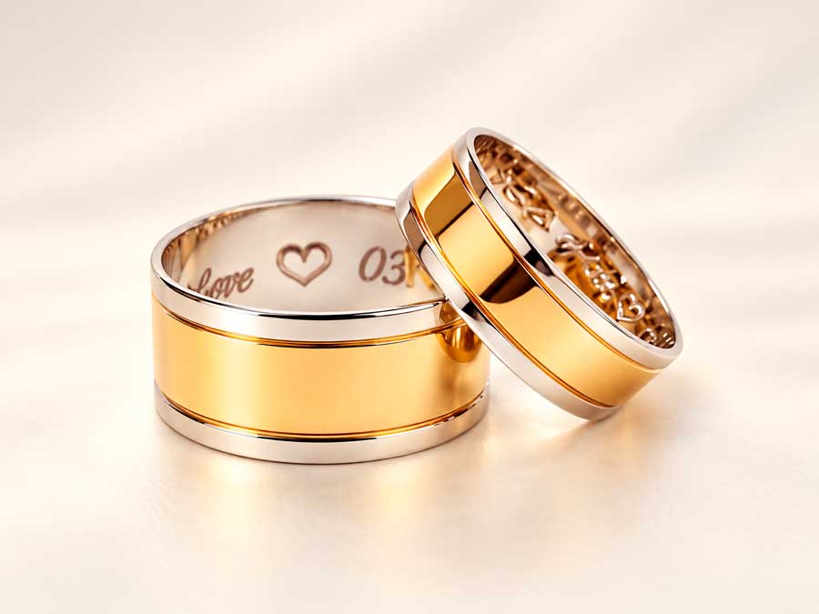 Brede vielsesringe i guld med blanke midterfelter og indvendig gravering med “love”, et hjerte og dato