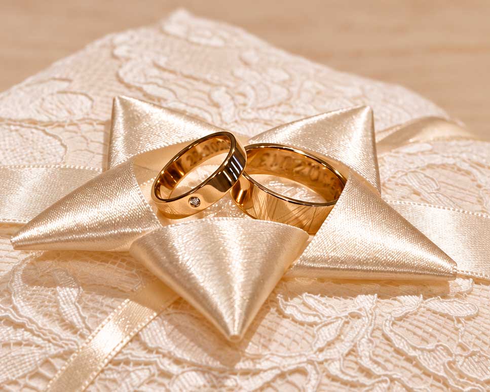 Vielsesringe i guld med håndgraveret mønster og en diamant i hendes ring, på en stjerneformet ringpude
