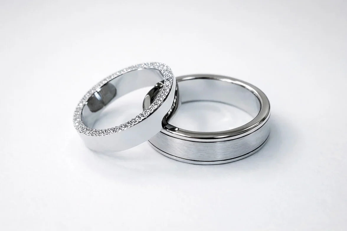 To vielsesringe i hvidguld, hendes ring med diamanter langs sidekanterne og hans med fine riller