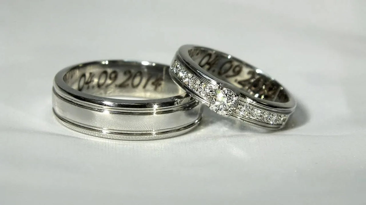 To vielsesringe i hvidguld med bryllupsdato indvendigt, hendes ring med diamanter og hans med fine riller