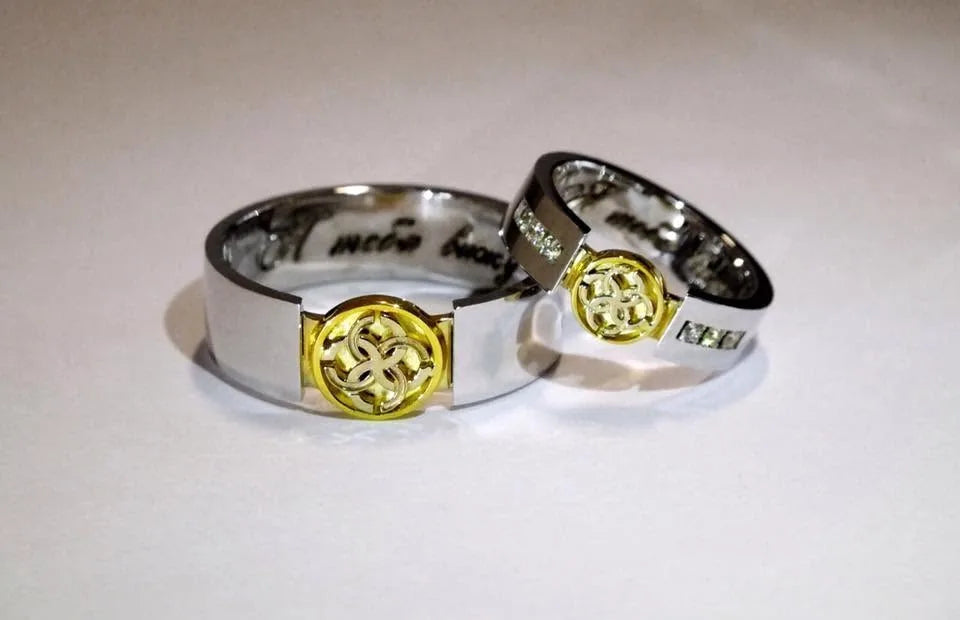 Vielsesringe i hvidguld og gult guld med et lille rundt symbol på forsiden og diamanter i hendes ring