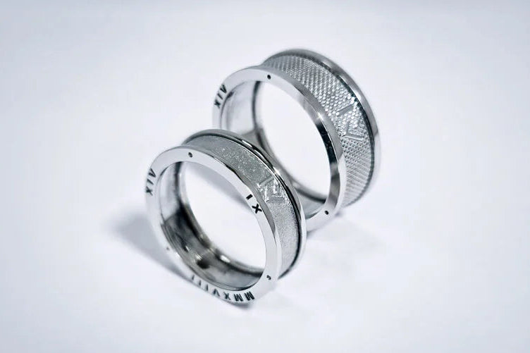 To vielsesringe i hvidguld med indgraverede symboler, en blank ring og en ring med mønstret overflade