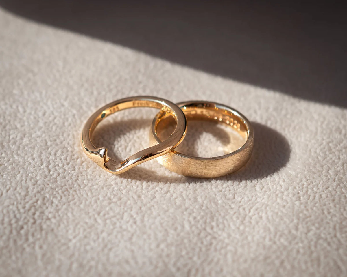 Vielsesringe i guld med en bred børstet ring og en bølget ring, formet til at følge forlovelsesringen