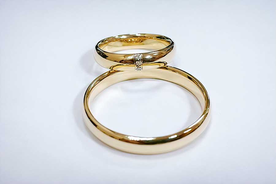 Klassiske vielsesringe i gult guld med tre diamanter i hendes ring, vist på en lys flade