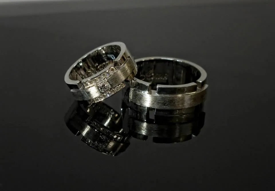 Brede vielsesringe i hvidguld med diamanter i hendes ring, vist på en sort spejlflade